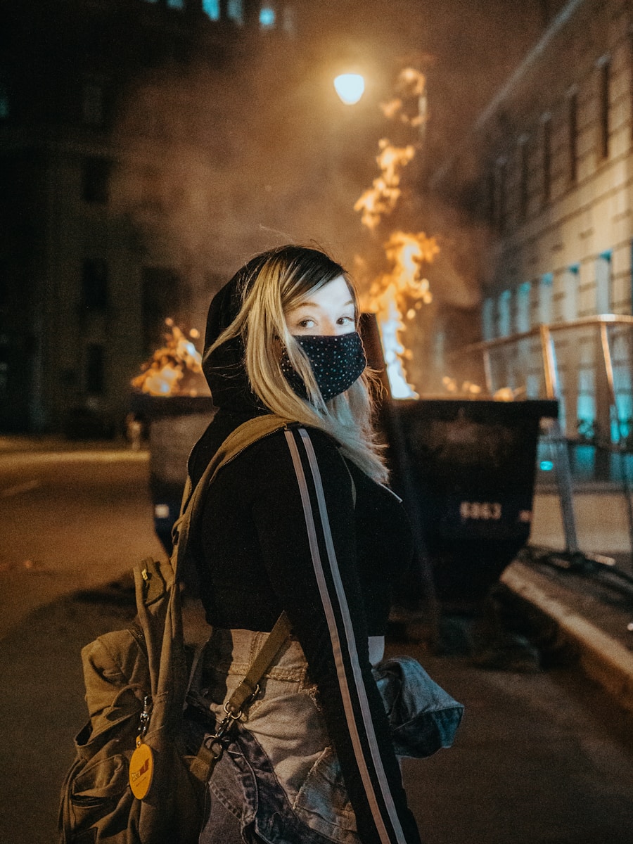 Photo by Amber Kipp woman in black and white mask and brown jacket standing on sidewalk during night time