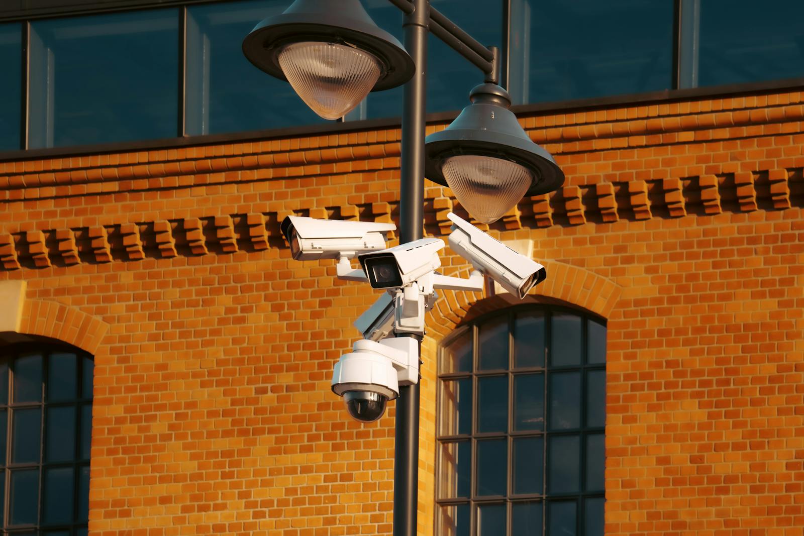 Photo by Jakub Zerdzicki Modern security cameras mounted on a pole against a brick building in the city.