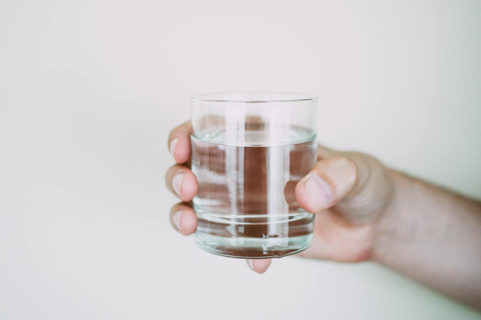Photo by Lisa from Pexels A close-up shot of a hand holding a clear glass of water, symbolizing refreshment.