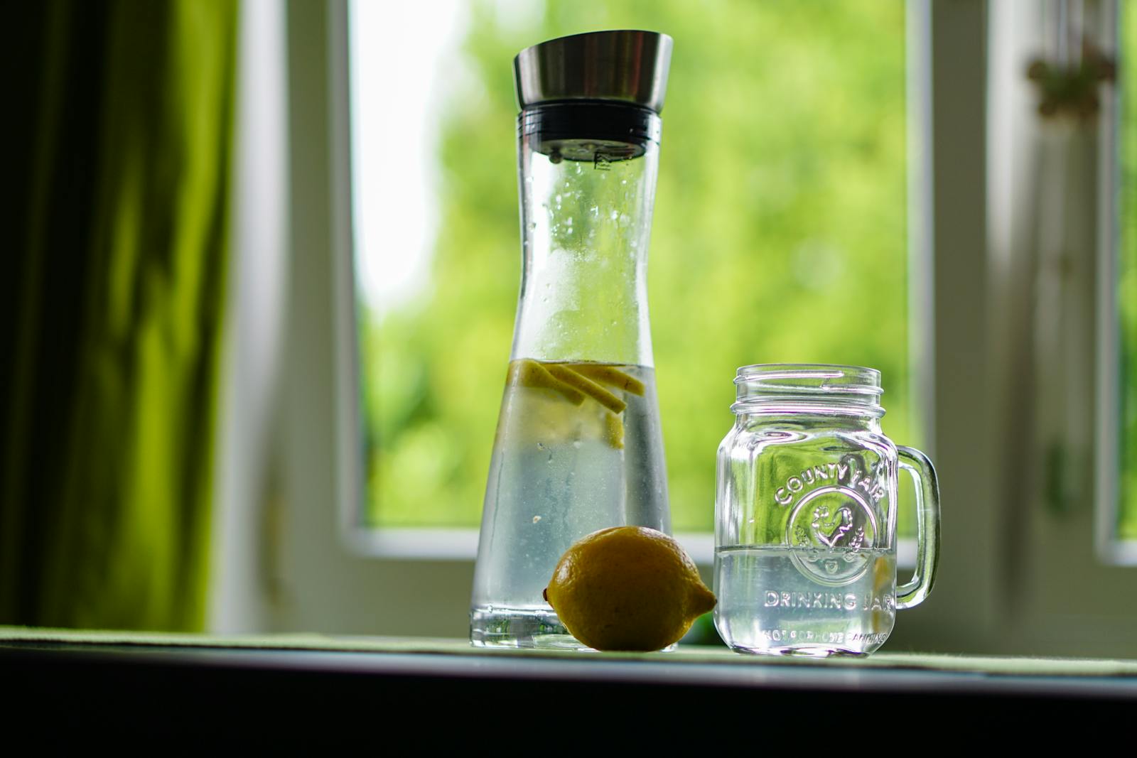 Photo by Pixabay Lemon-infused water in a glass carafe and mason jar on a windowsill, evoking freshness.