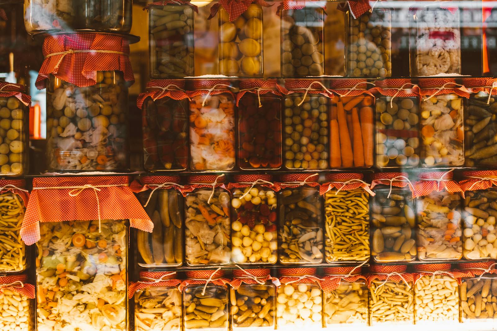 Photo by ROMAN ODINTSOV Rows of colorful preserved vegetables in glass jars, showcasing variety and abundance.