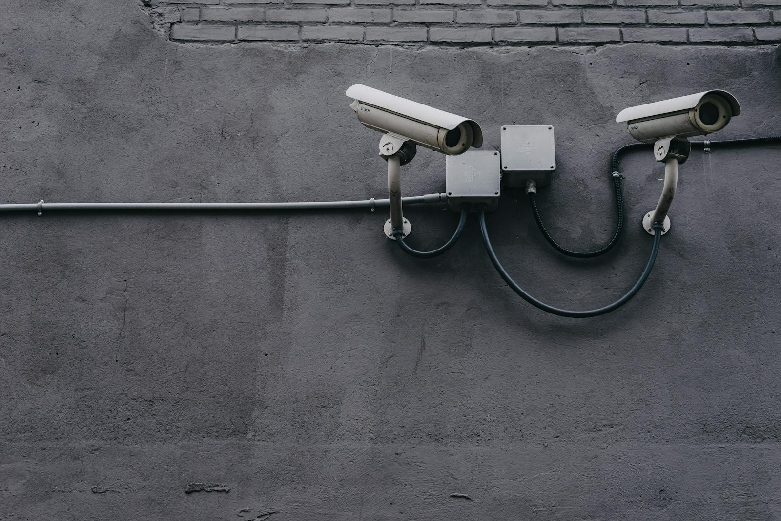 Photo by Scott Webb Two surveillance cameras mounted on a concrete wall, highlighting security technology.