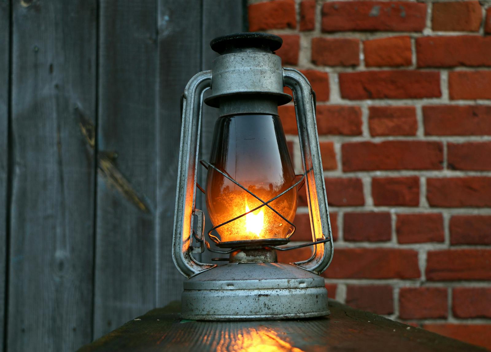 Photo by Pixabay Close-up of an antique oil lantern casting a warm glow against a rustic red brick wall.