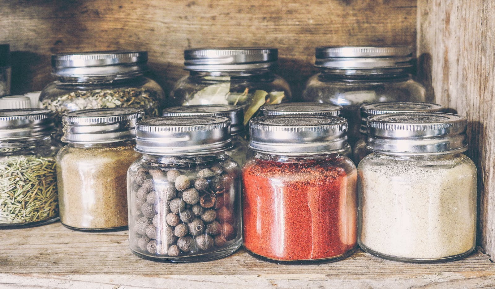 Photo by monicore A collection of assorted spices in glass jars on a rustic wooden shelf for culinary use.