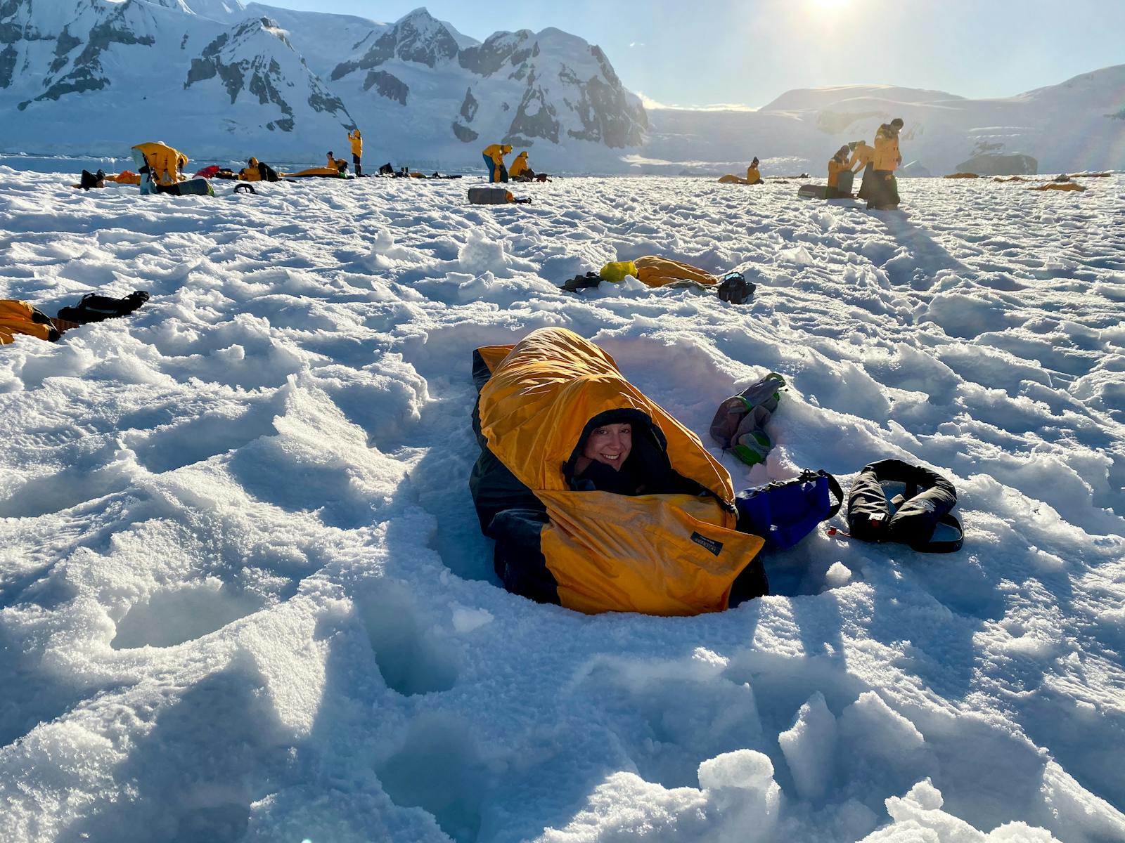 Smiling woman in a sleeping bag during a camping expedition on Antarctica's snowy terrain.