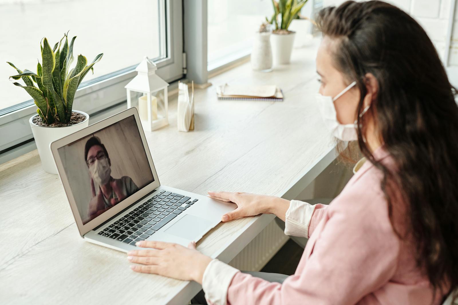 Photo by Edward Jenner Woman and doctor video calling on laptop, both wearing masks, symbolizing telehealth during COVID-19.