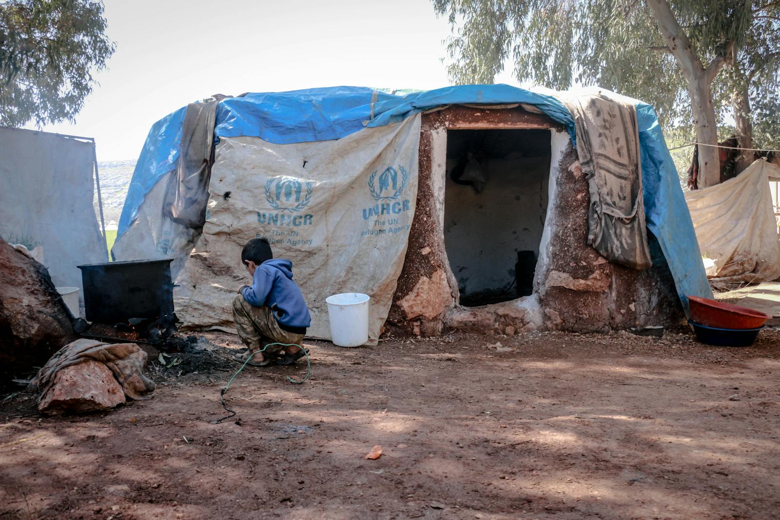 Photo by Ahmed akacha An outdoor scene showing a boy near a makeshift shelter in Idlib, highlighting living conditions.