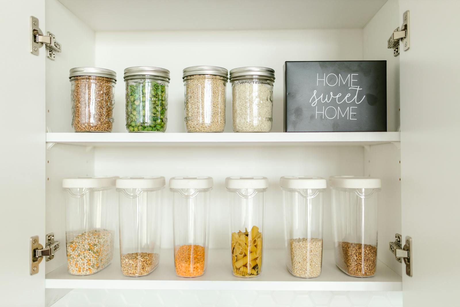 Photo by RDNE Stock project Neatly arranged glass and plastic jars containing grains and pasta in a kitchen cabinet.