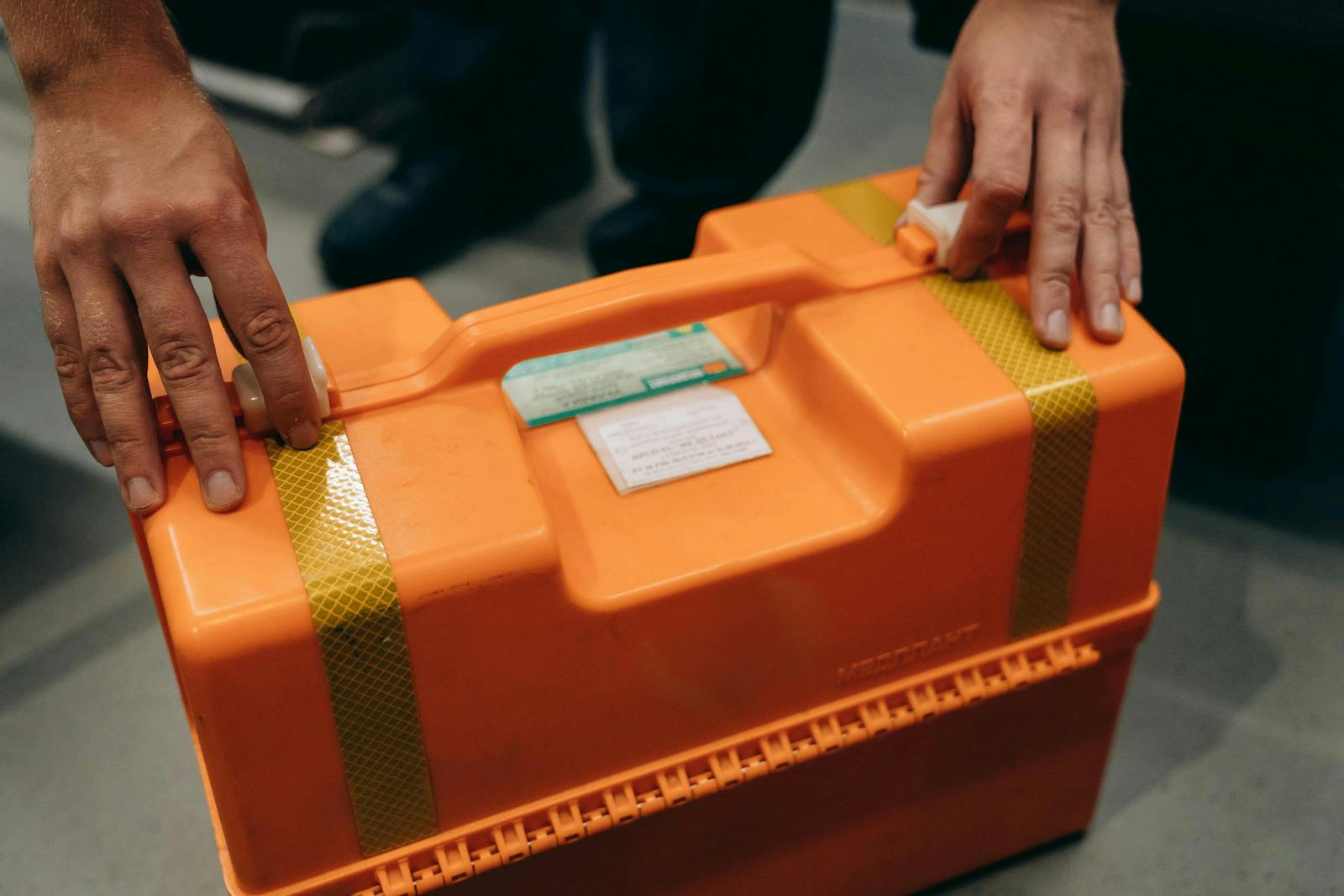 Photo by Mikhail Nilov Close-up of hands holding an orange emergency medical kit indoors.