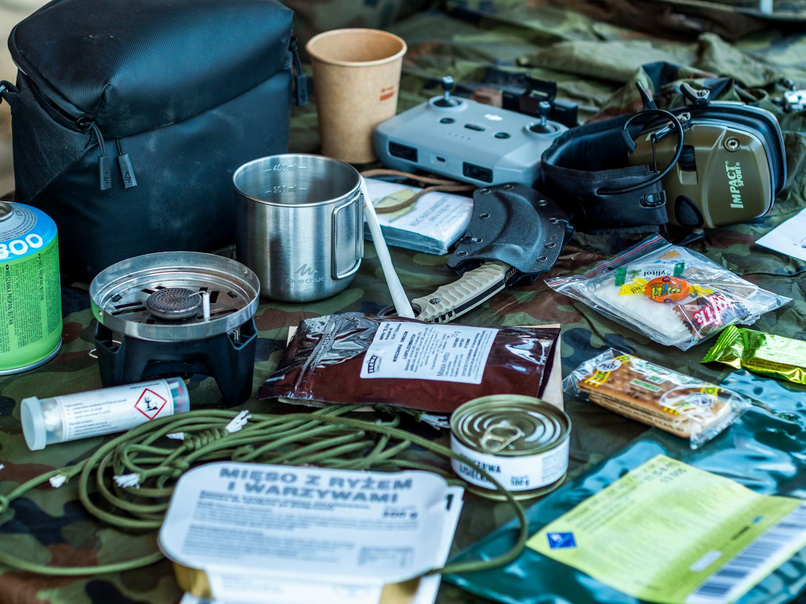 A diverse assortment of camping and survival items laid out, including food, tools, and gadgets.